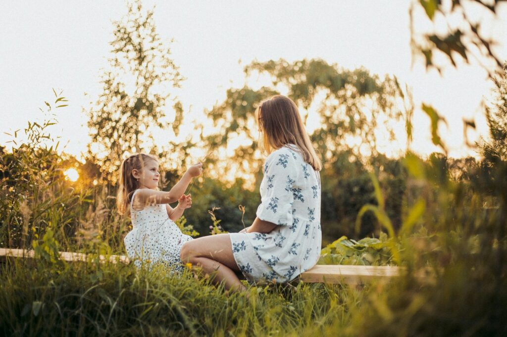 Moeder en dochter zitten samen buiten in het gras bij avondzon
